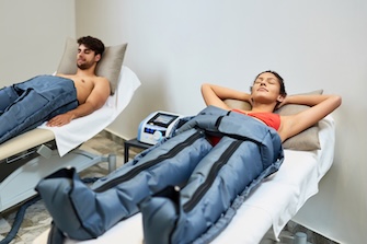 Young couple relaxing during pressotherapy at health spa. Focus is on woman.